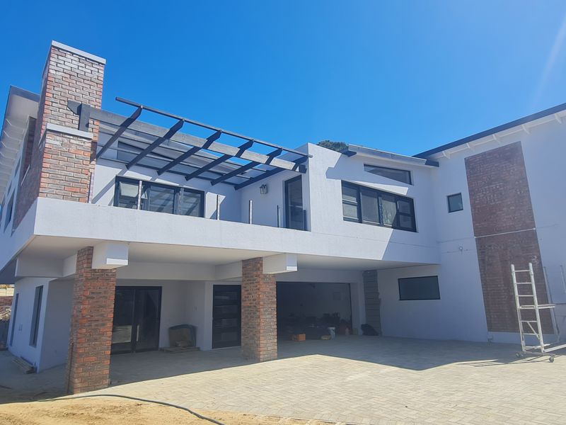 Rear view of a modern duet property featuring a paved driveway, brick accents, a balcony with a pergola, and unfinished surrounding landscaping.