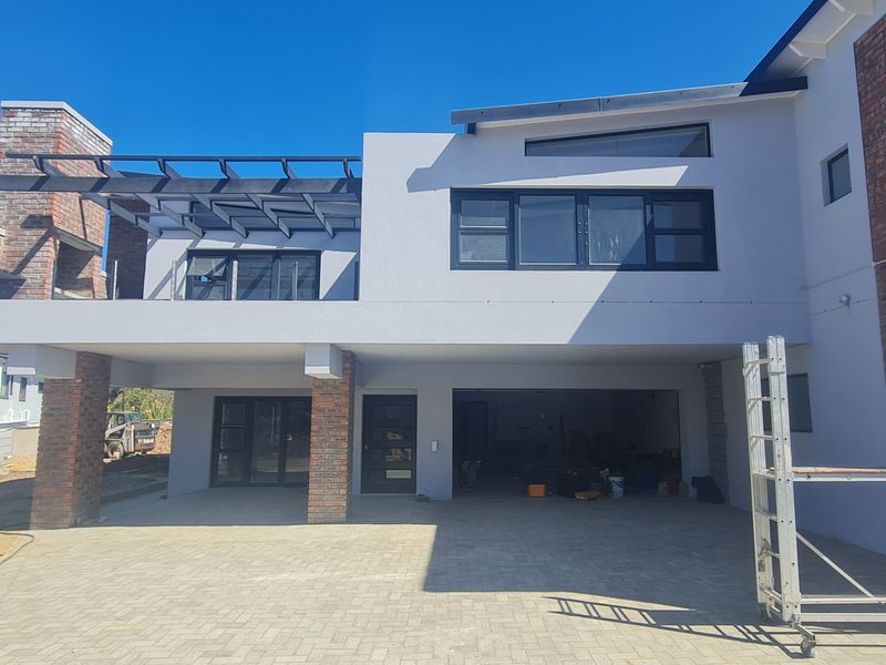Rear elevation of a duet property featuring a covered patio, brick accents, pergola structure, and paved driveway area currently under final construction stages.