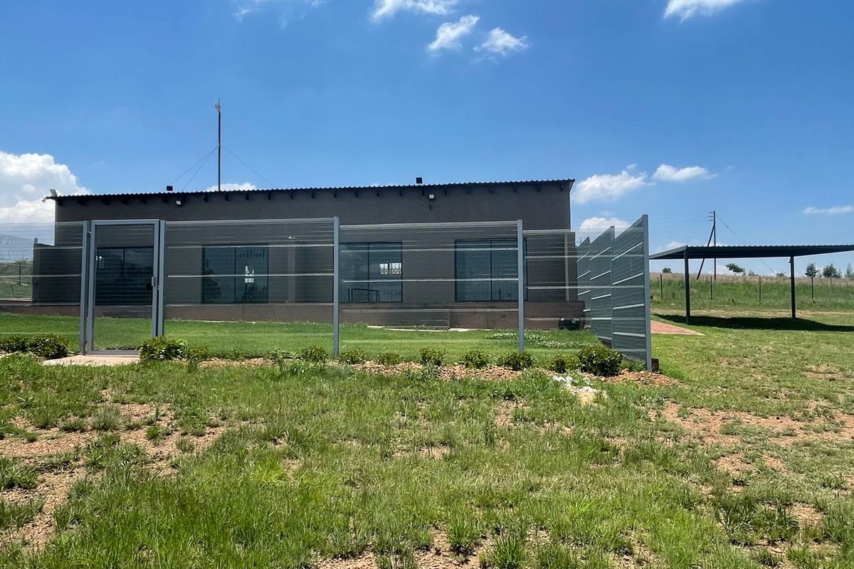 Rear view of the cottage featuring a fenced yard, sliding glass doors, and a detached metal carport structure on the property.