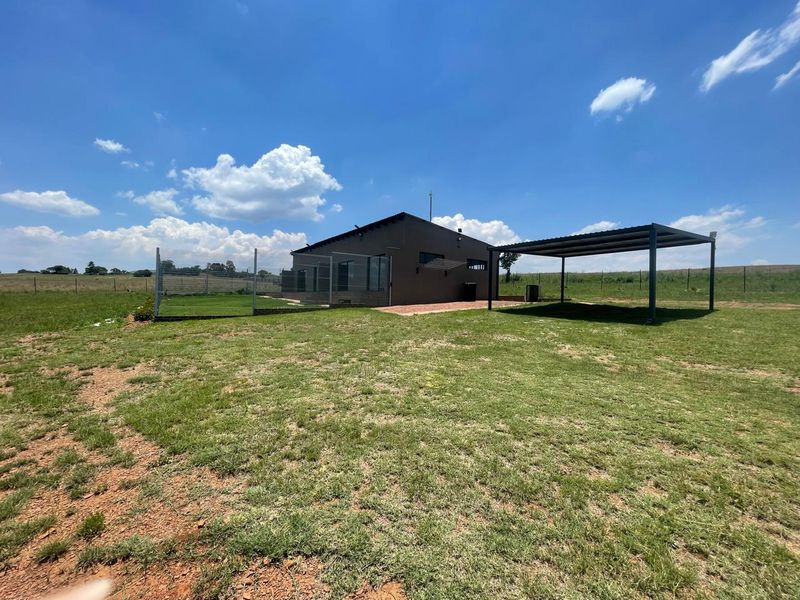 Rear view of the cottage featuring a spacious lawn, a detached metal carport, and a fenced garden area with a paved patio.