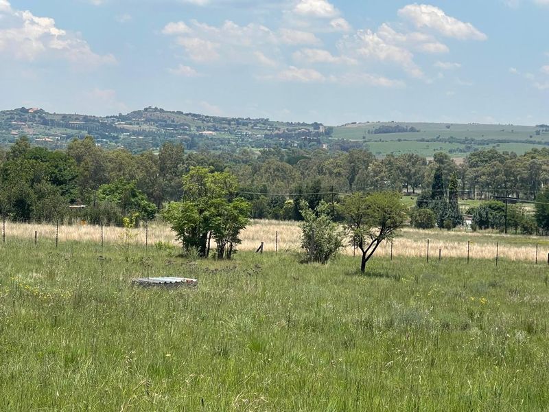 A scenic view of the surrounding landscape and open fields, featuring established trees and perimeter electric fencing.
