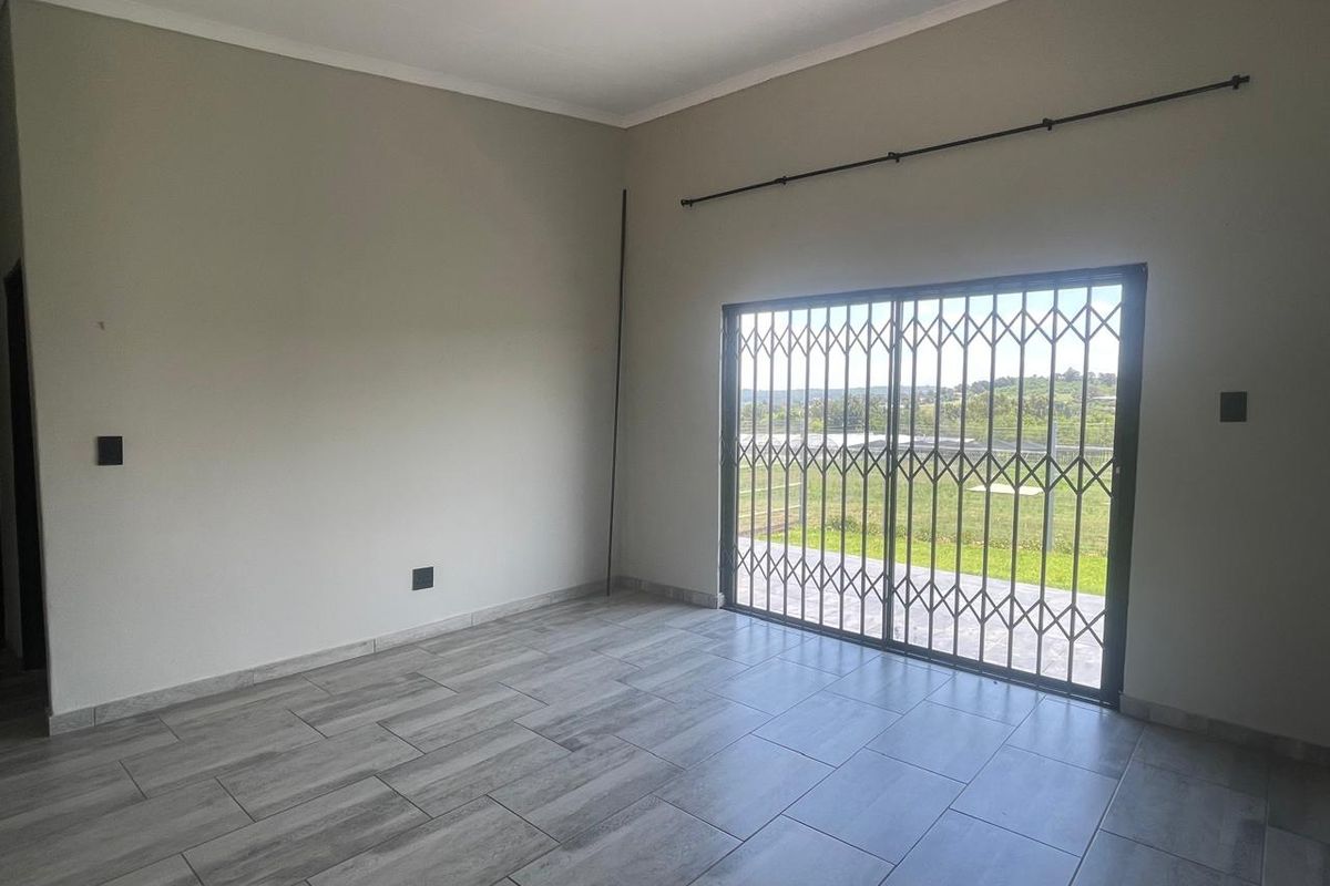 A bright, empty living room featuring modern grey tiled flooring and a sliding glass door with a security gate leading to the outdoors.