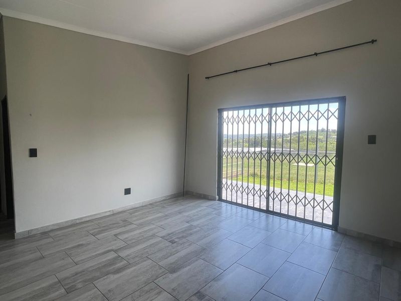 A bright, empty living room featuring modern grey tiled flooring and a sliding glass door with a security gate leading to the outdoors.