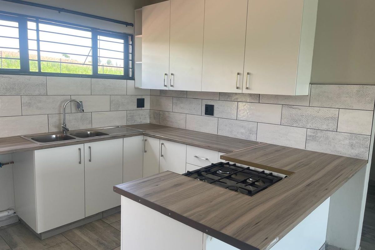 A clean, modern kitchen featuring white cabinetry, wood-look laminate countertops, a gas hob, and a tiled backsplash with a double sink.