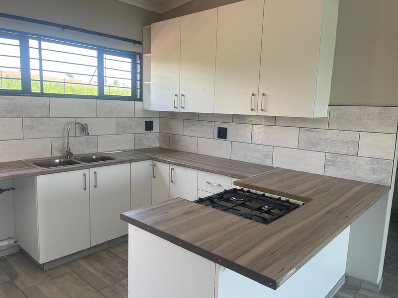 A clean, modern kitchen featuring white cabinetry, wood-look laminate countertops, a gas hob, and a tiled backsplash with a double sink.