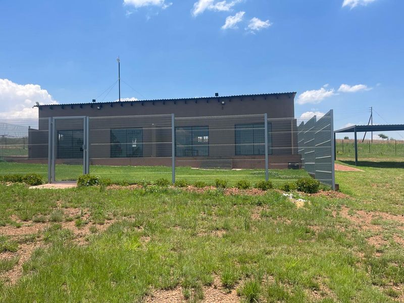 Rear view of the cottage featuring a large lawn, secure mesh fencing, and multiple sliding glass doors providing access to the interior.