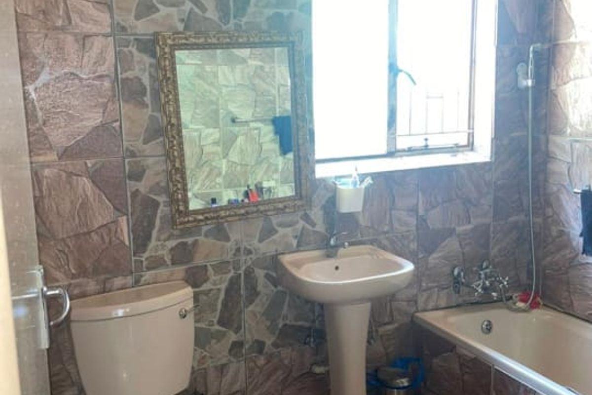 A dated bathroom featuring a pedestal basin, toilet, and bathtub with extensive stone-style wall and floor tiling.