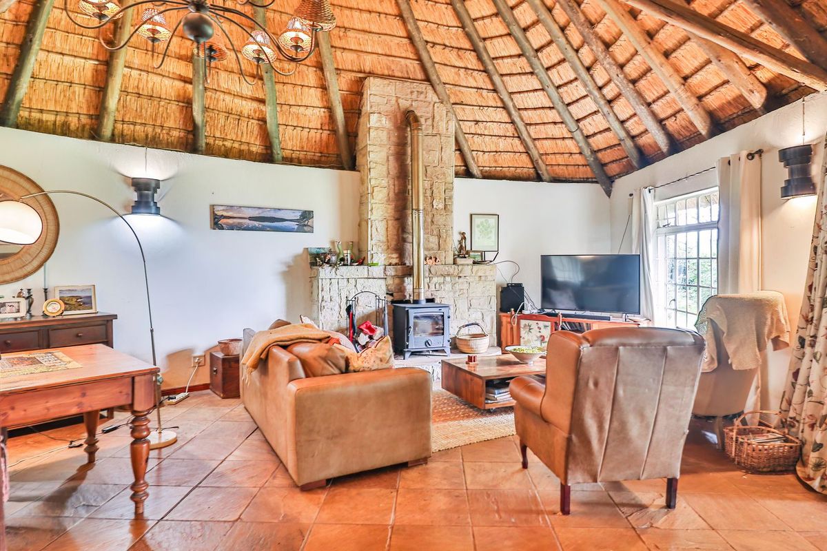 A cozy living room featuring a high vaulted thatched ceiling with exposed rafters, terracotta flooring, and a prominent stone fireplace with a wood-burning stove.