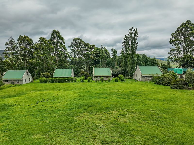 A wide-angle view of multiple detached cottage-style dwellings set within a large, well-maintained green lawn area with mature trees in the background.