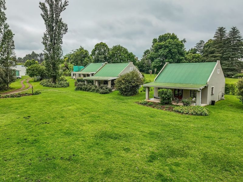 A view of two detached residential cottages featuring green corrugated metal roofs and covered patios set within a spacious, well-maintained garden.