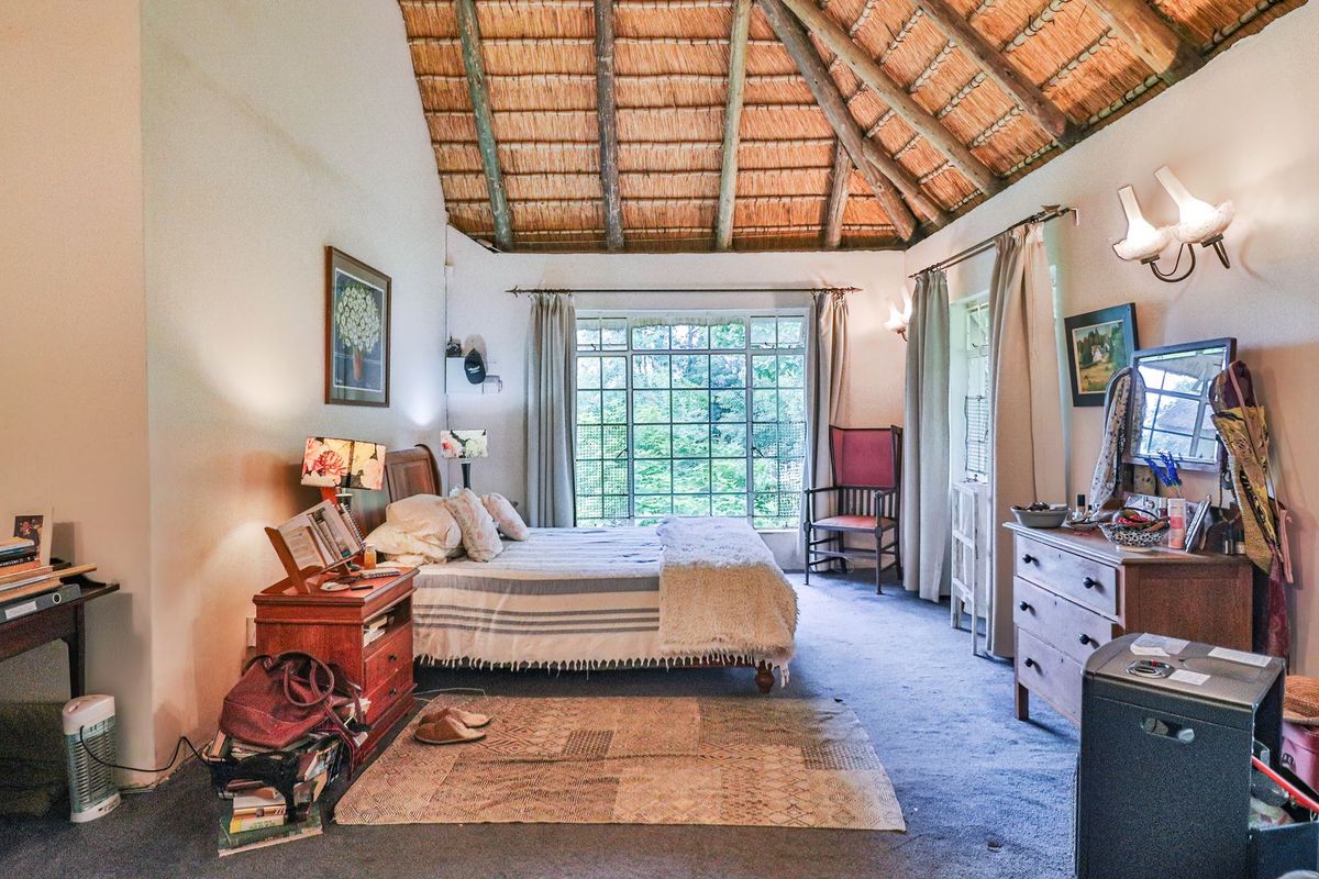 Spacious bedroom featuring a high vaulted ceiling with exposed timber rafters and a traditional thatched roof, complemented by large windows overlooking greenery.
