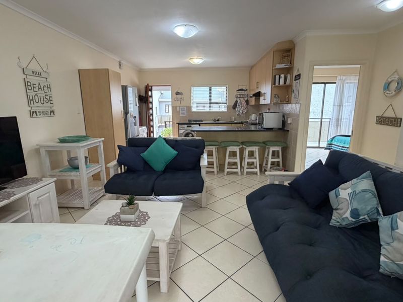 Open-plan living and kitchen area featuring tiled flooring, a breakfast bar, and functional cabinetry, creating a cohesive and practical living space.