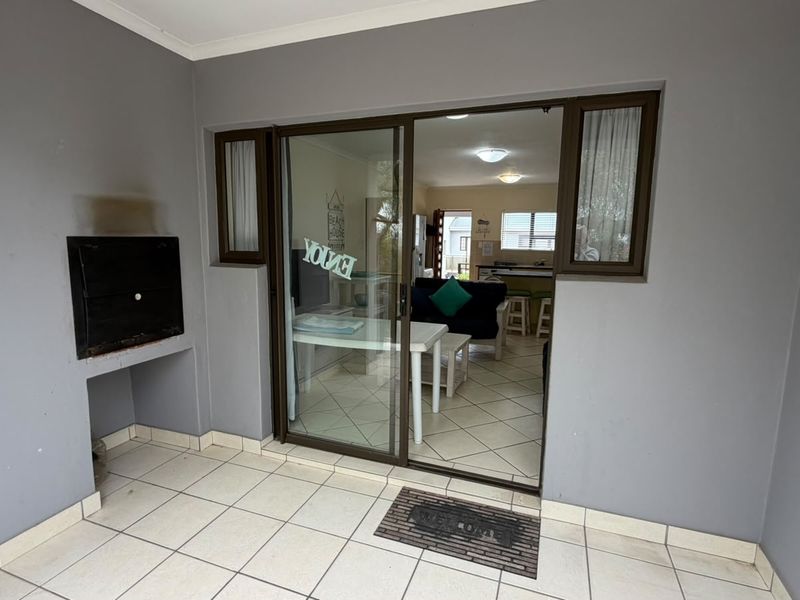 Covered patio area featuring a built-in braai, tiled flooring, and sliding glass door access to the interior living space.