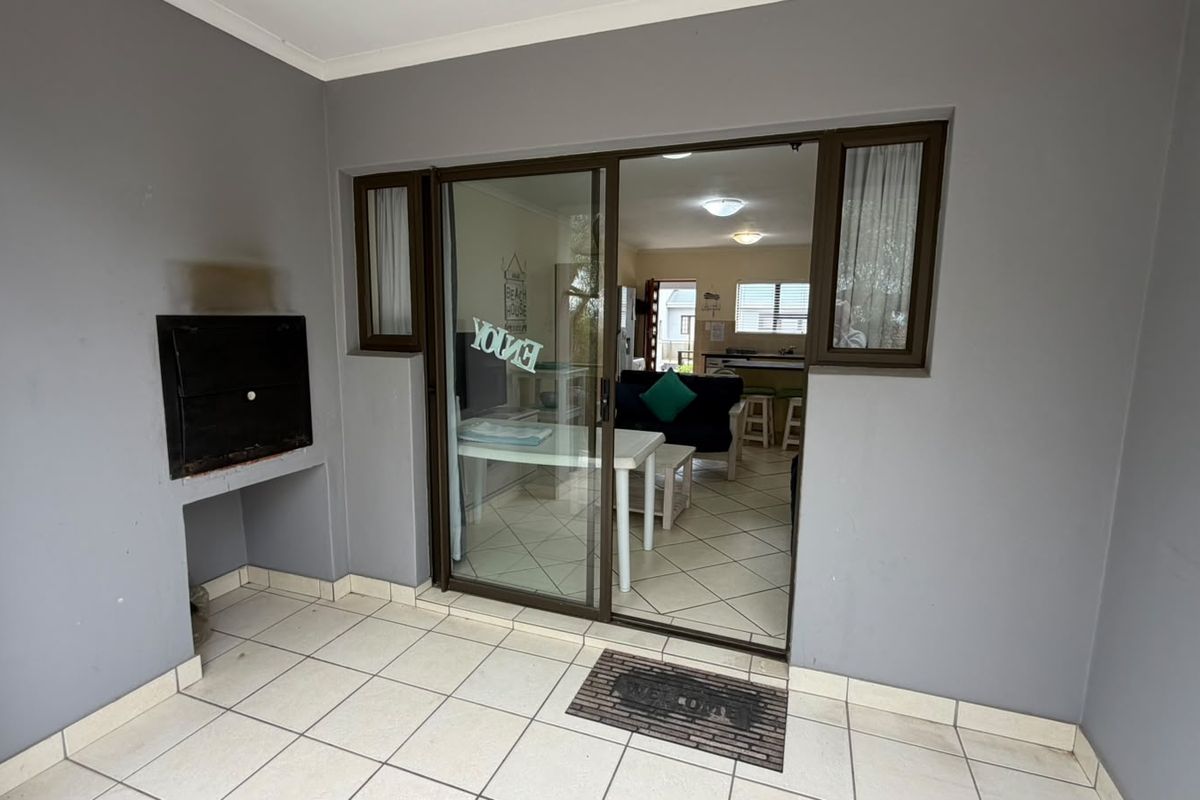 Covered patio area featuring a built-in braai, tiled flooring, and sliding glass door access to the interior living space.