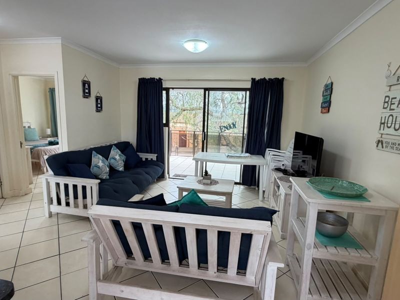 A bright living room featuring tiled flooring and a sliding glass door providing access to an outdoor balcony area.