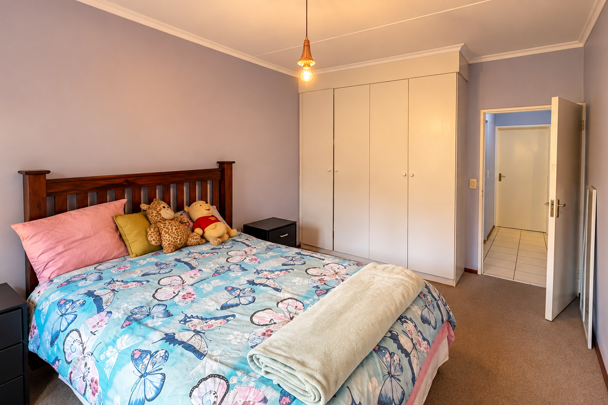 A well-lit bedroom featuring built-in cupboards, neutral wall finishes, and carpeted flooring, providing a functional and comfortable living space.