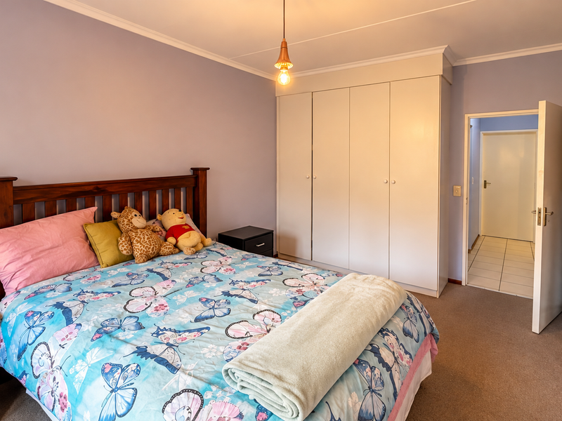 A well-lit bedroom featuring built-in cupboards, neutral wall finishes, and carpeted flooring, providing a functional and comfortable living space.
