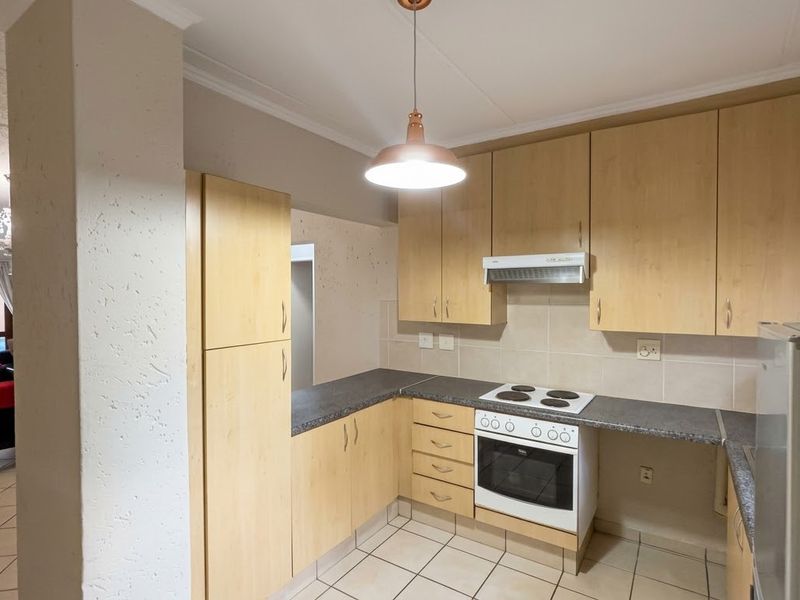 Functional kitchen featuring light wood-finish cabinetry, laminate countertops, built-in oven with hob, and tiled flooring, opening into the adjacent living area.