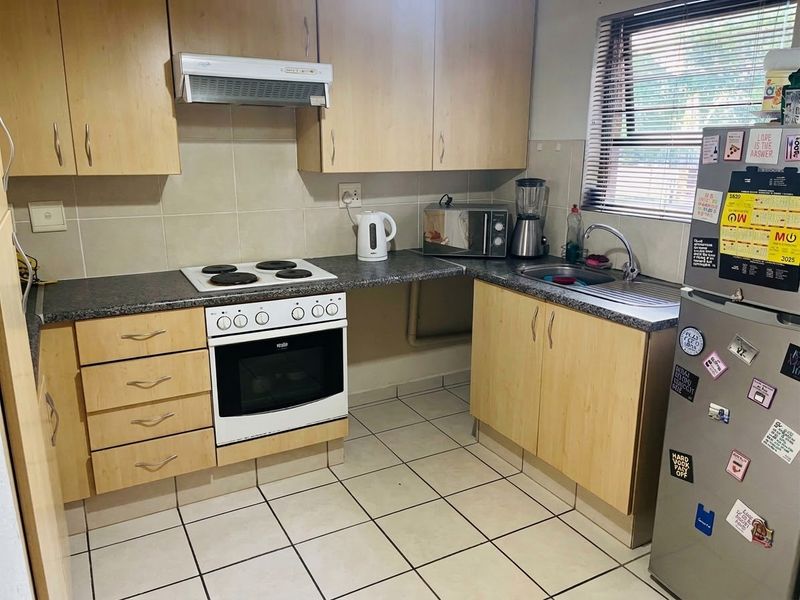 A functional kitchen featuring light wood-finish cabinetry, dark laminate countertops, a built-in electric stove with oven, and tiled flooring.