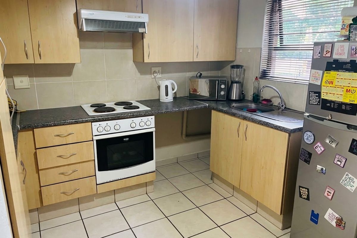 A functional kitchen featuring light wood-finish cabinetry, dark laminate countertops, a built-in electric stove with oven, and tiled flooring.