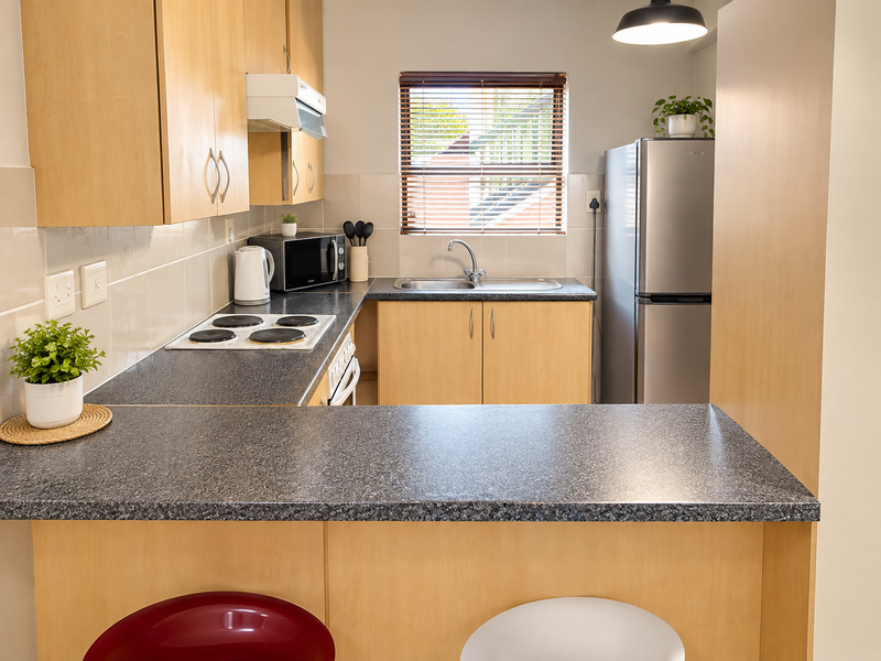A functional kitchen featuring light wood cabinetry, dark laminate countertops, a breakfast bar, and integrated electric hob with extractor fan.