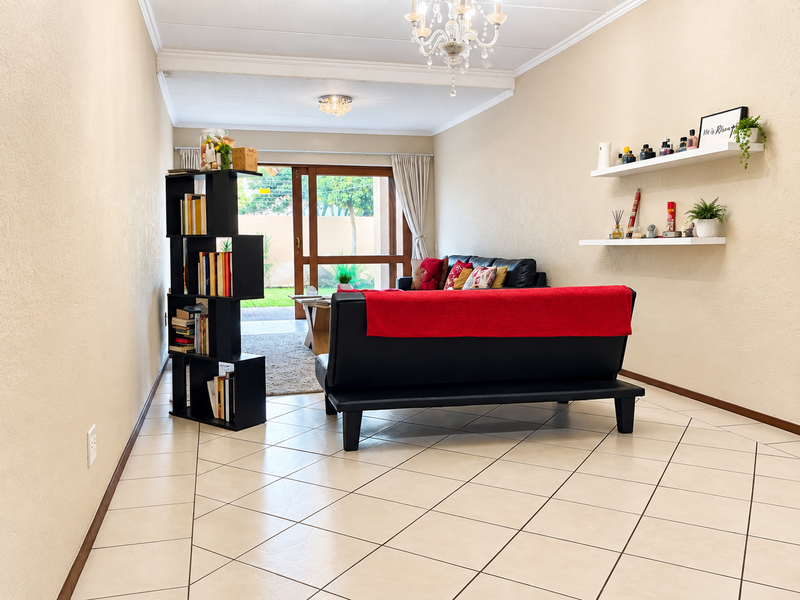 A bright living room featuring tiled flooring, dual ceiling light fixtures, and a sliding glass door providing access to the outdoor area.