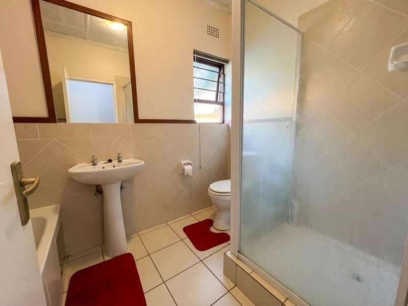 A functional bathroom featuring a pedestal basin, toilet, and a glass-enclosed shower with tiled finishes throughout.
