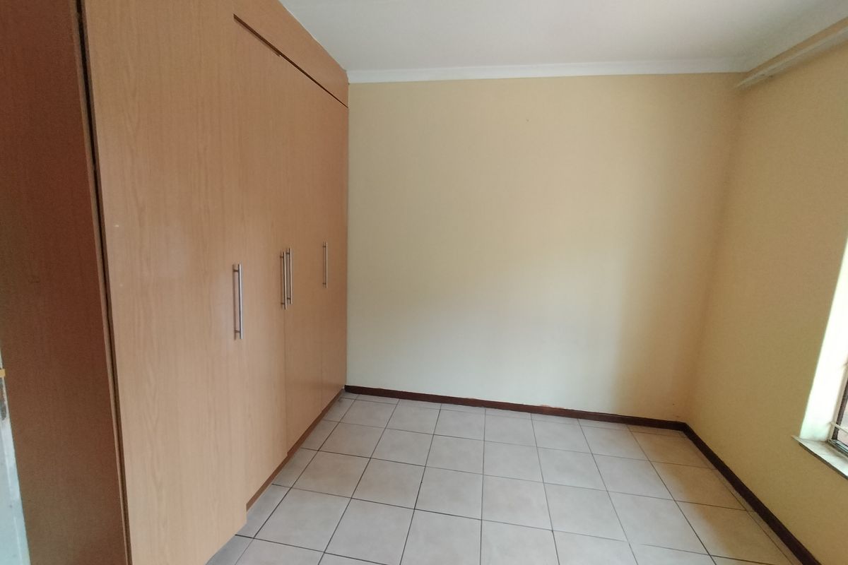 A clean, empty bedroom featuring neutral tiled flooring and ample built-in wooden cupboards, offering a blank canvas for personalization.