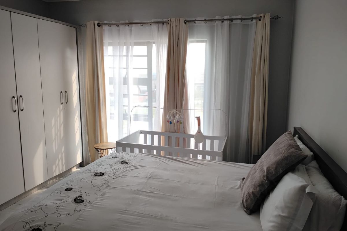 A well-lit bedroom featuring built-in cupboards and large windows with curtain rails, providing a functional and comfortable living space.