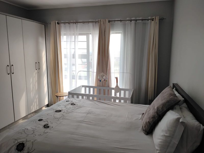 A well-lit bedroom featuring built-in cupboards and large windows with curtain rails, providing a functional and comfortable living space.