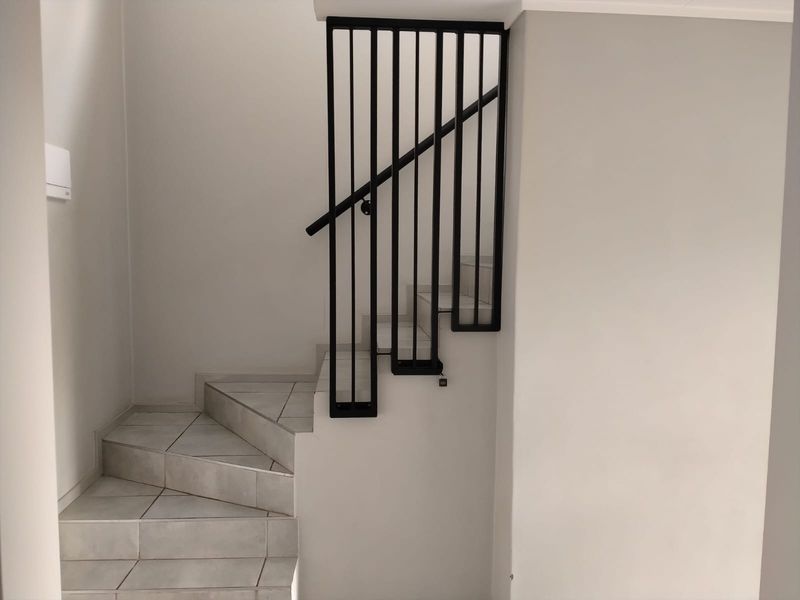 A clean, modern staircase featuring light-colored floor tiles and a minimalist black metal balustrade with a matching handrail.