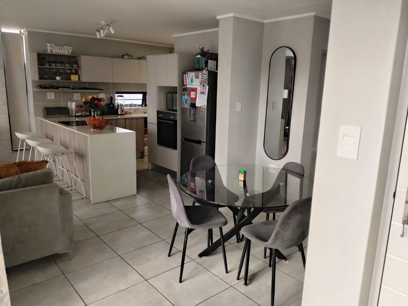 Open-plan living and dining area featuring a modern kitchen with a central island, built-in oven, and neutral tiled flooring throughout.