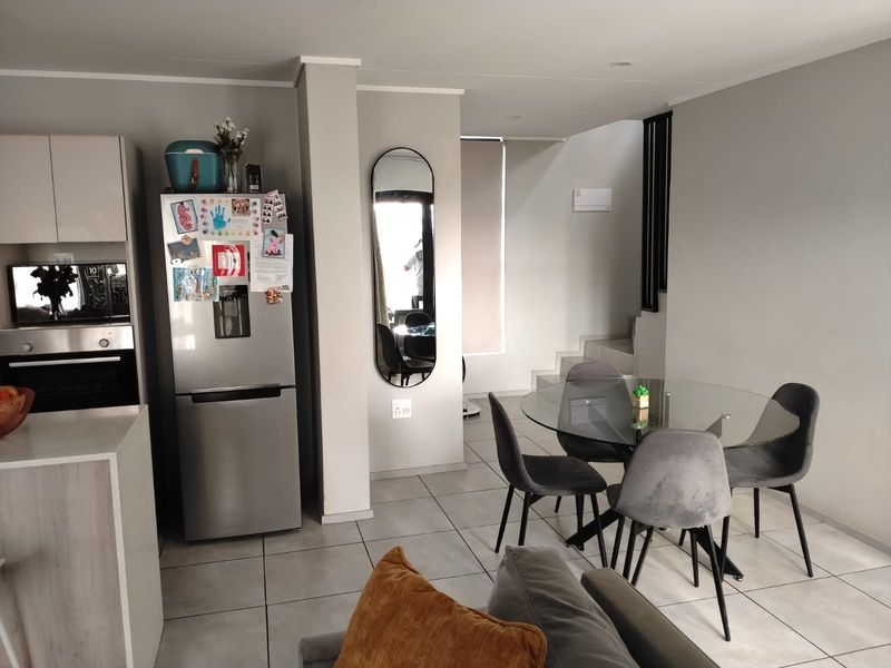 Open-plan living and dining area featuring tiled flooring, modern cabinetry, built-in oven, and a staircase leading to the upper level.