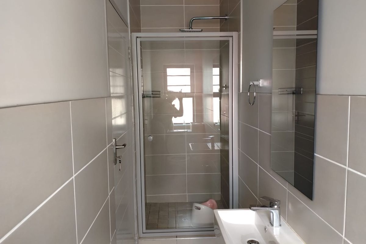 A clean, modern bathroom featuring a glass-enclosed shower, wall-mounted basin with mixer tap, and neutral wall tiling.