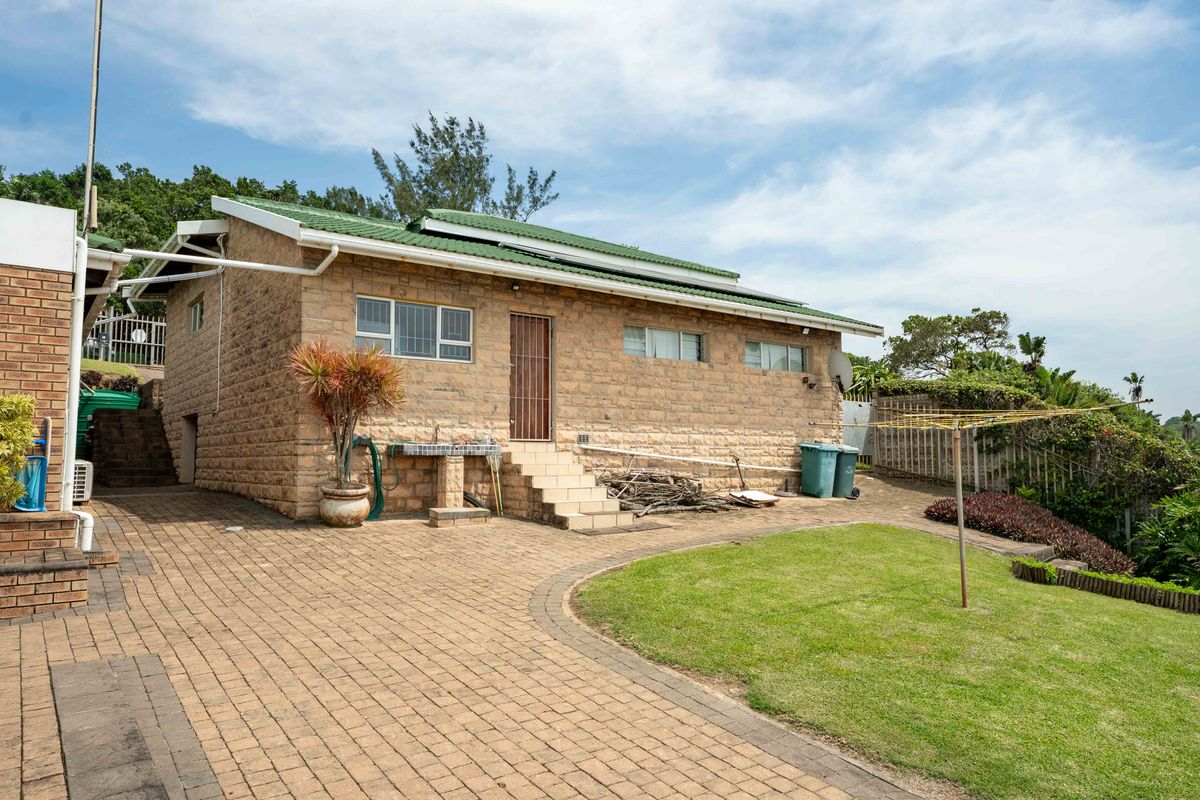 Rear view of a brick-clad house featuring a green metal roof, paved driveway, and a small lawn area with an external wash basin.