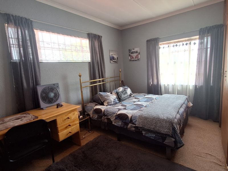 A functional bedroom featuring built-in cabinetry, dual windows with curtains, and carpeted flooring.