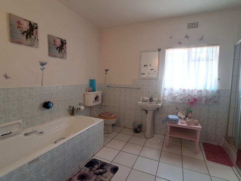A functional bathroom featuring a bathtub, pedestal basin, and toilet with classic tiled finishes and natural light from a window.