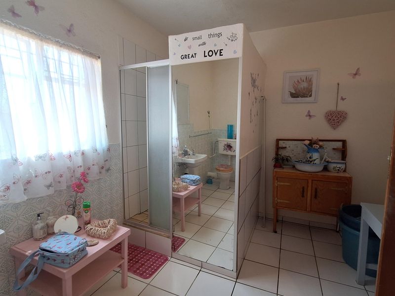 A functional bathroom featuring a shower enclosure, pedestal basin, and toilet, with tiled flooring and partial wall tiling.