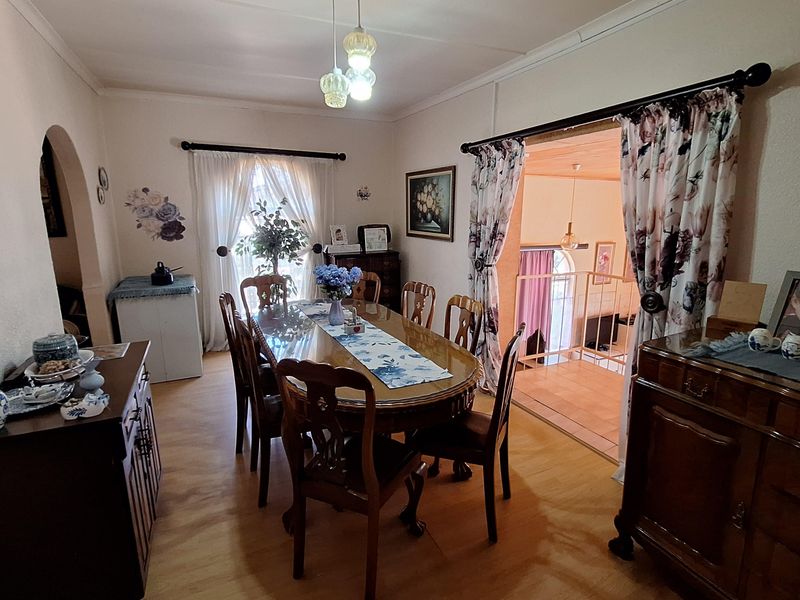 A traditional dining room featuring wood-look flooring, a central pendant light fixture, and an arched entryway leading to an adjacent living space.