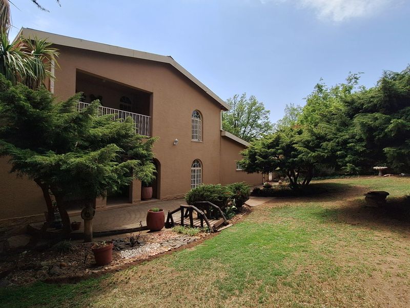 A view of the rear exterior of the house, featuring a covered patio, landscaped garden, and mature trees.