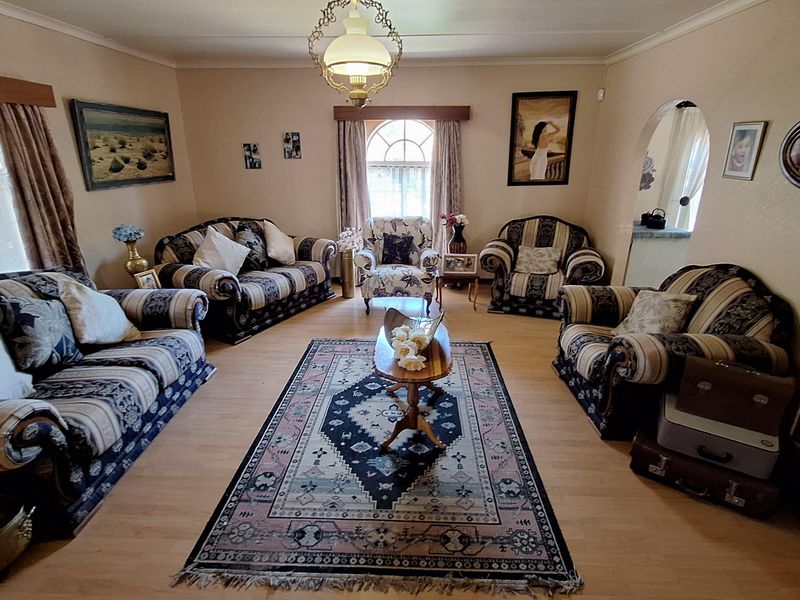 A traditional living room featuring light-toned laminate flooring, a central pendant light fixture, and an arched doorway leading to an adjacent space.