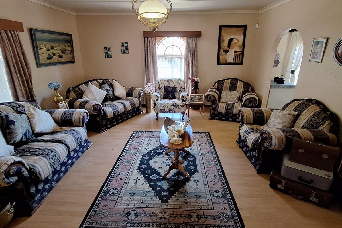 A traditional living room featuring light-toned laminate flooring, a central pendant light fixture, and an arched doorway leading to an adjacent space.