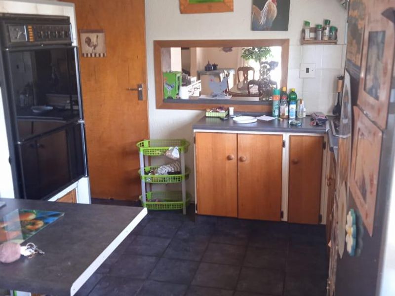A dated kitchen featuring wood-finish cabinetry, a built-in wall oven, dark tiled flooring, and a serving hatch opening into the adjacent living area.