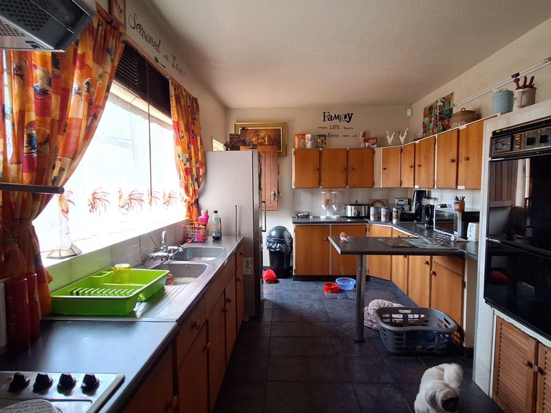A dated kitchen featuring wooden cabinetry, integrated oven, and dark floor tiles, offering a functional layout with significant potential for modernization.