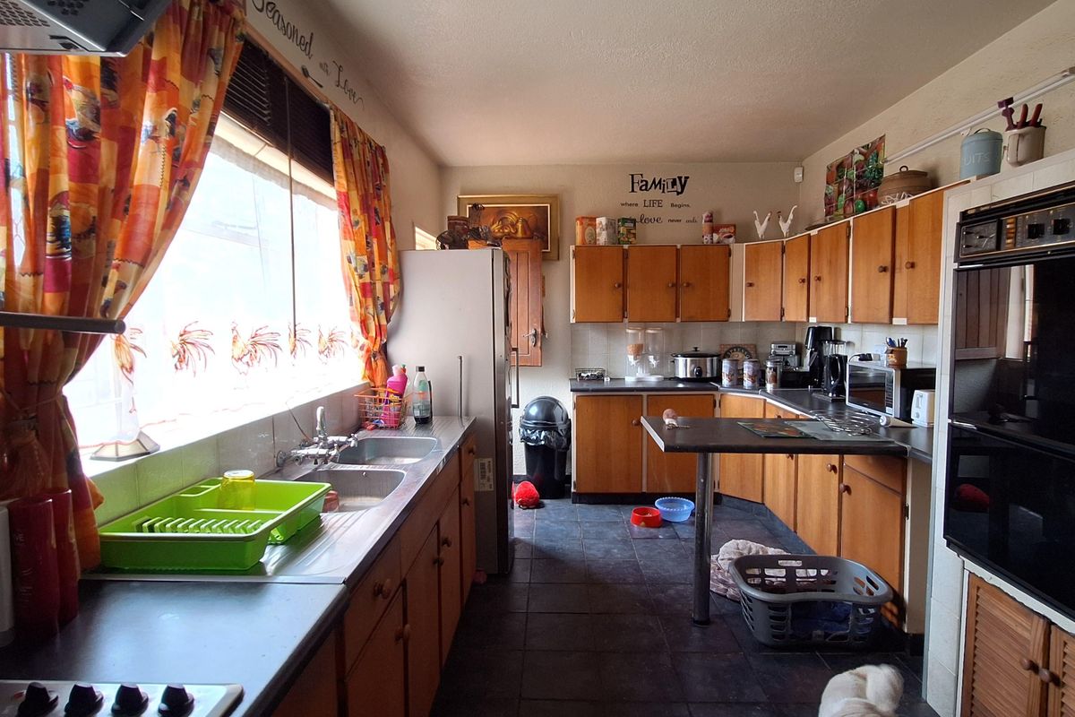A dated kitchen featuring wooden cabinetry, integrated oven, and dark floor tiles, offering a functional layout with significant potential for modernization.
