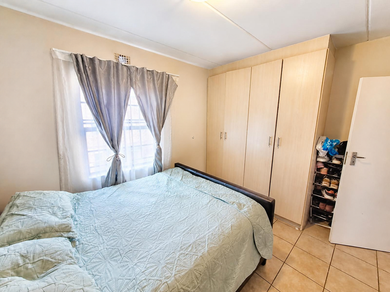 A functional bedroom featuring built-in wooden cupboards, tiled flooring, and a window with security bars, providing a practical and well-lit living space.