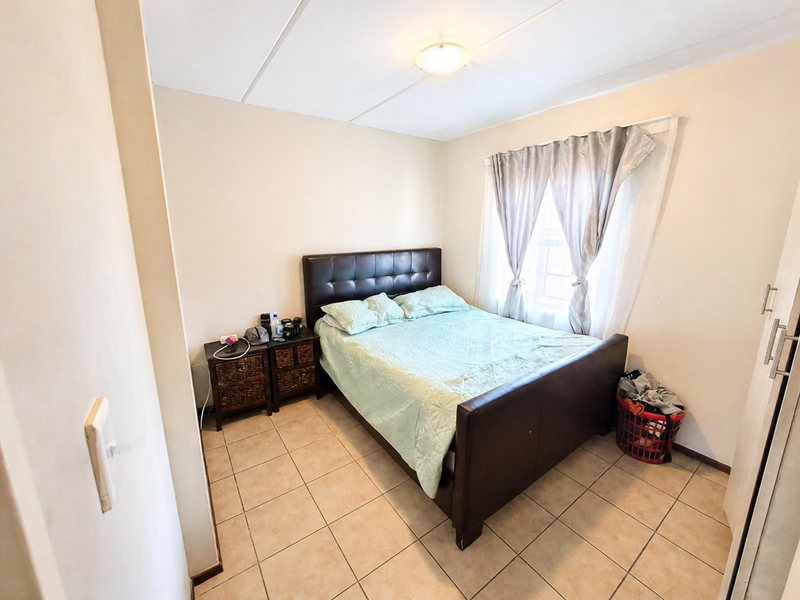A functional bedroom featuring tiled flooring, a built-in wardrobe, and a window with curtains, providing a comfortable living space.