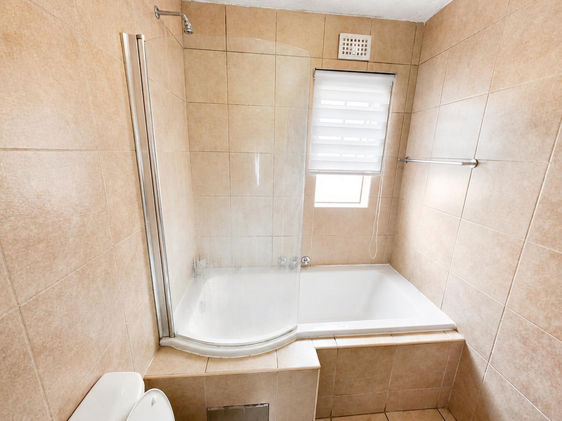 A functional bathroom featuring a built-in bathtub with a glass shower screen, tiled walls, and neutral finishes.
