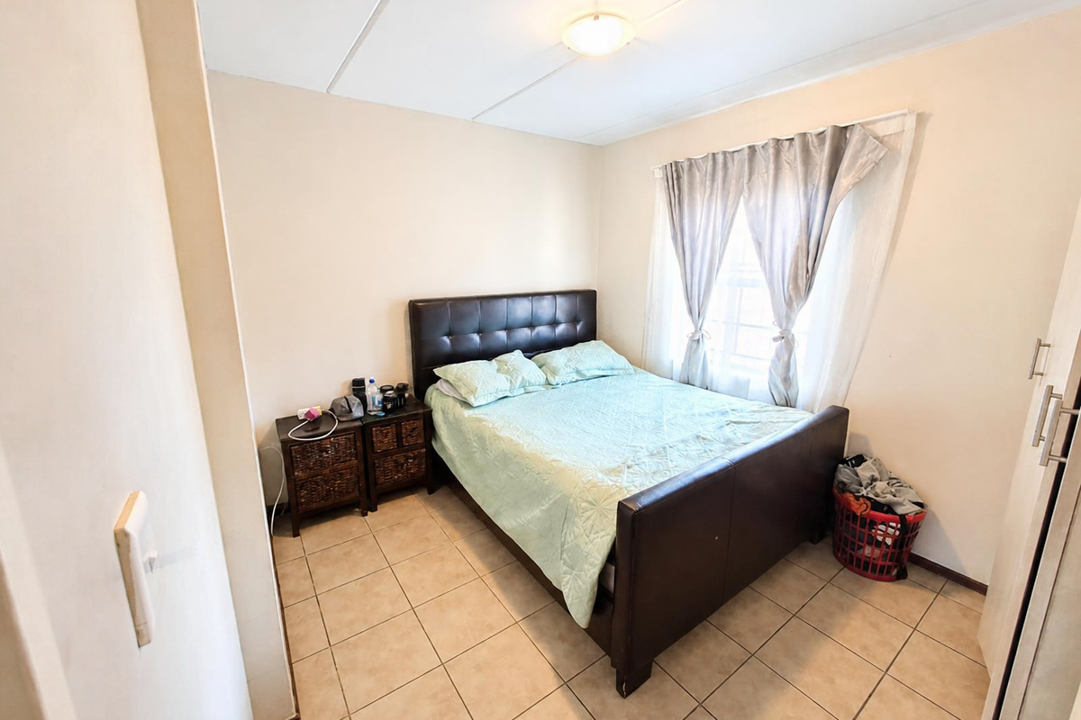 A functional bedroom featuring tiled flooring, a built-in wardrobe, and a window with curtains, providing a comfortable living space.