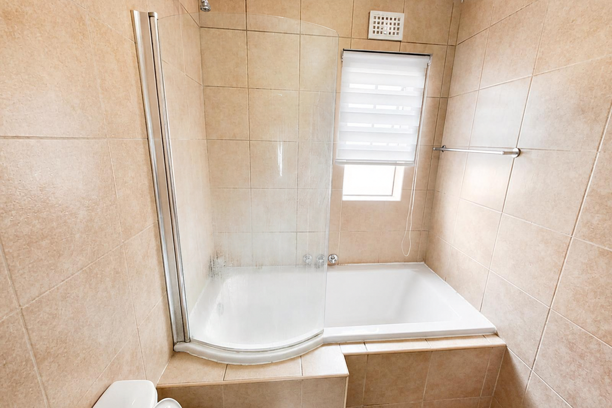 A functional bathroom featuring a built-in bathtub with a glass shower screen, tiled walls, and neutral finishes.